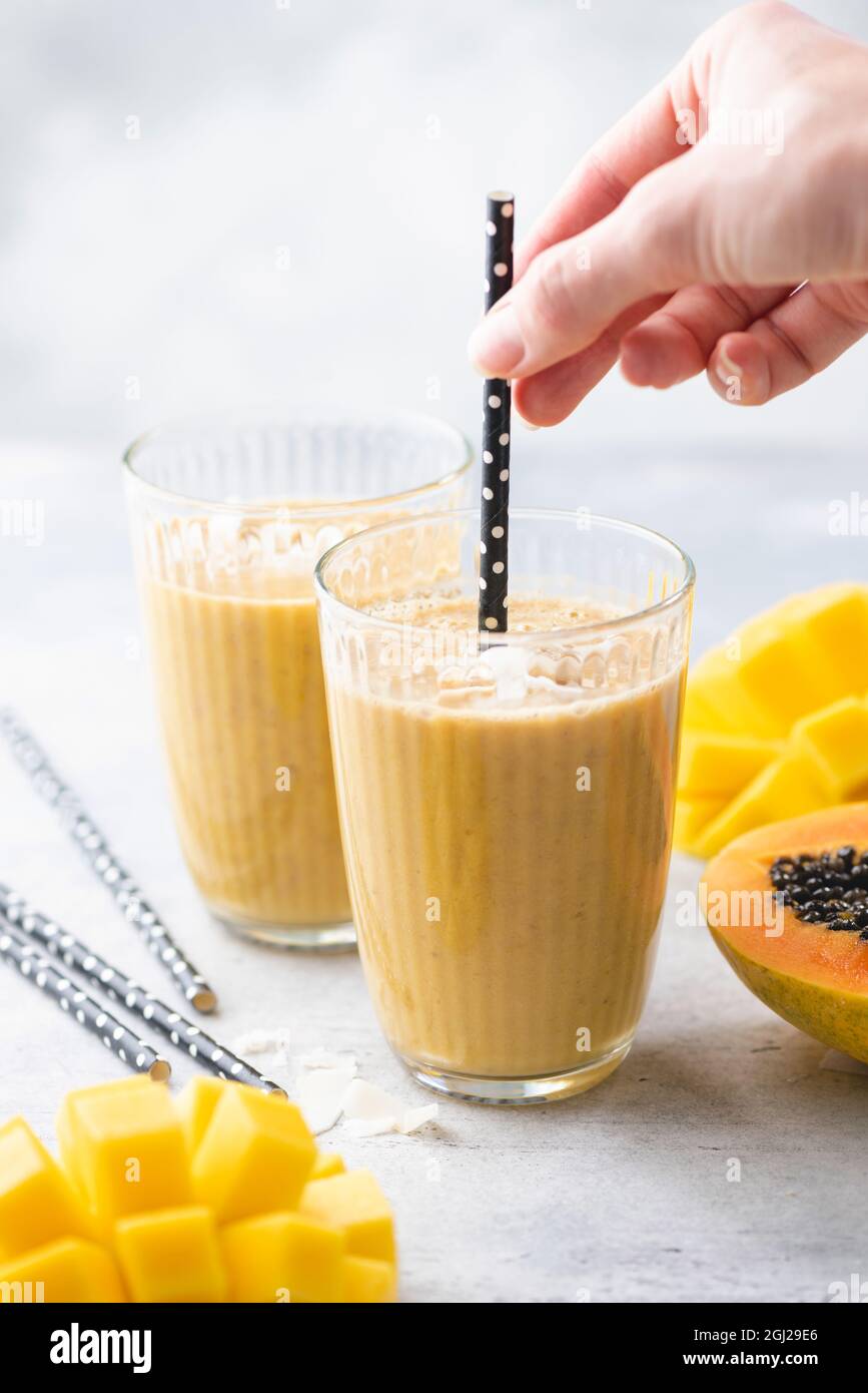 Tropischer Mango-Kokosnuss-Smoothie in einem Glas mit Papiertrinkstroh, Nahaufnahme Stockfoto