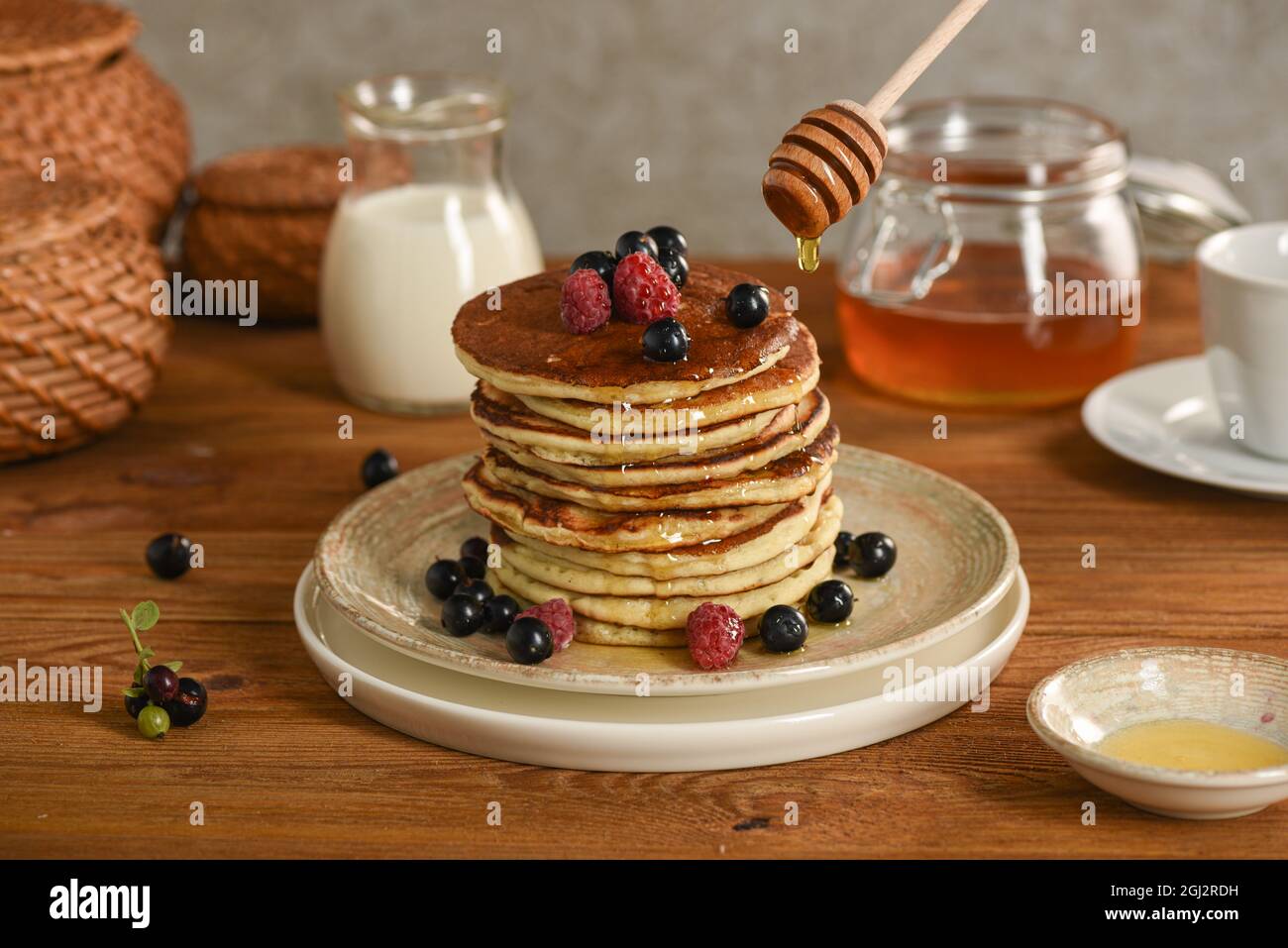 Amerikanische Pfannkuchen mit Honig und Rahm. Schwarze Johannisbeere, Himbeere, Brombeere mit Beeren bestreut. Selektiver Fokus Stockfoto