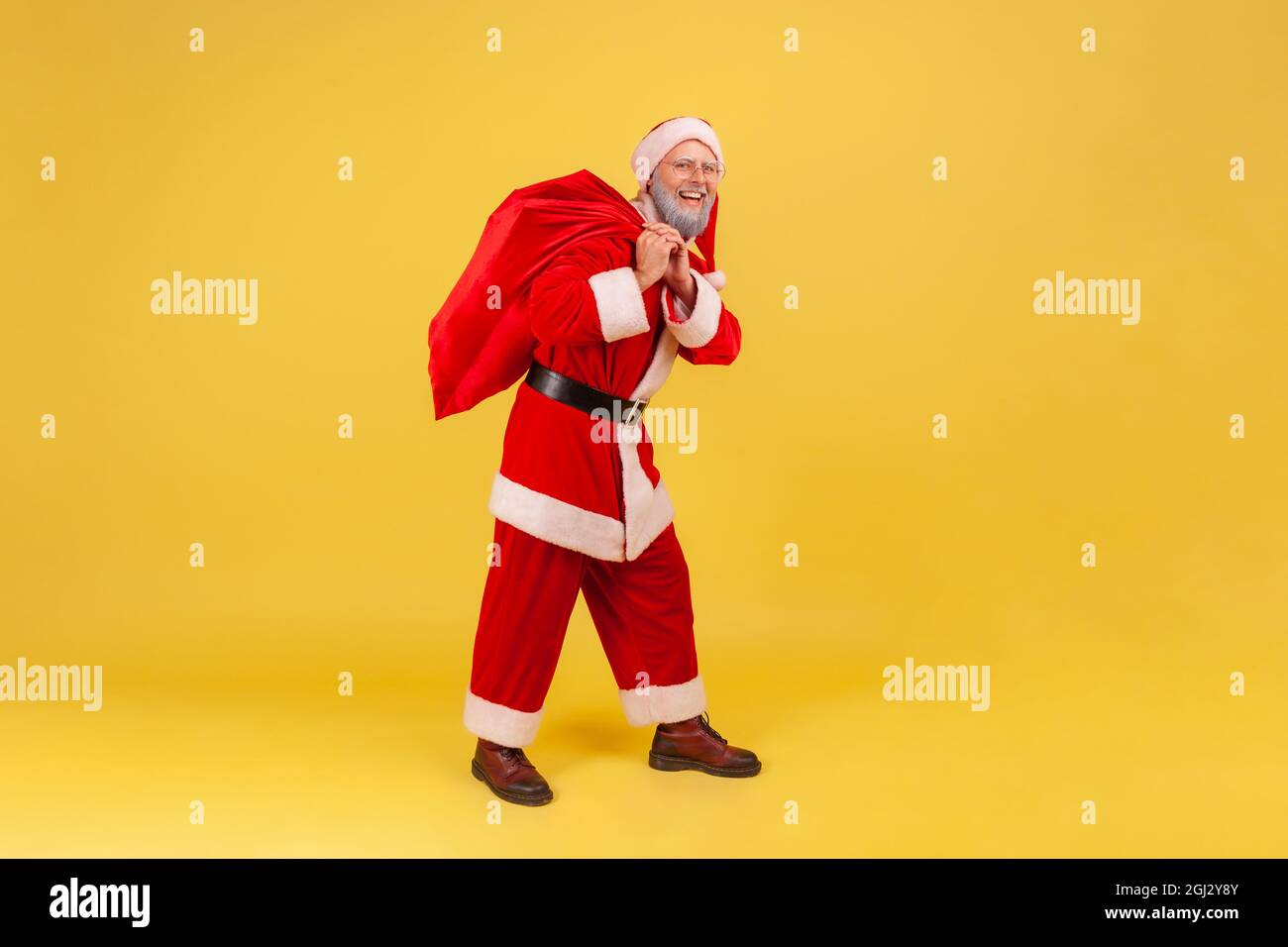 In voller Länge Porträt eines älteren Mannes mit grauem Bart trägt weihnachtsmann Kostüm stehend mit großen roten Tasche mit Geschenken für Weihnachtsferien. Innen Stockfoto