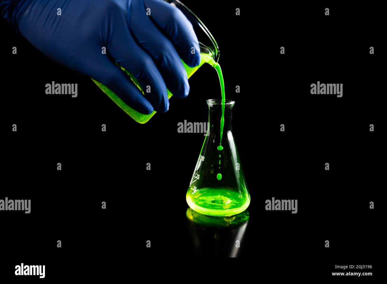 Ein Wissenschaftler, der in einem dunklen biomedizinischen Labor für die Gesundheitsmedizin mit grünen fluoreszierenden Tröpfchen in einer konischen Glaskolben experimentiert d Stockfoto