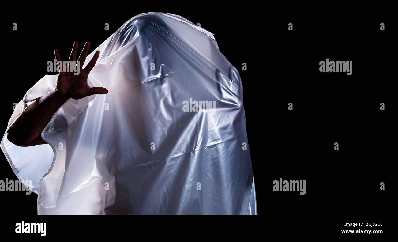 Ein Mann, der wie ein Geist mit einem weißen Grabtuch bedeckt ist, zeigt Entsetzen isoliert auf schwarzem Hintergrund Stockfoto