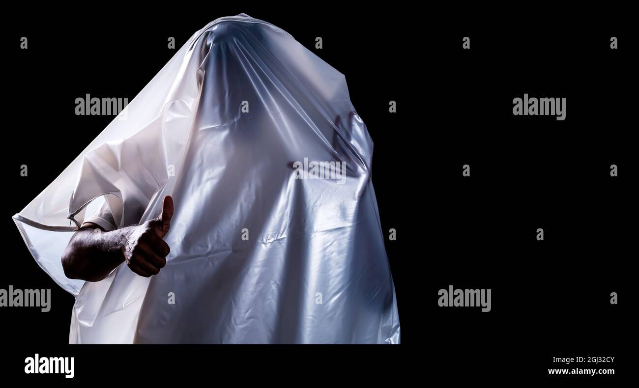 Ein Mann, der wie ein Geist mit einem weißen Grabtuch bedeckt ist, zeigt einen Daumen isoliert auf schwarzem Hintergrund Stockfoto