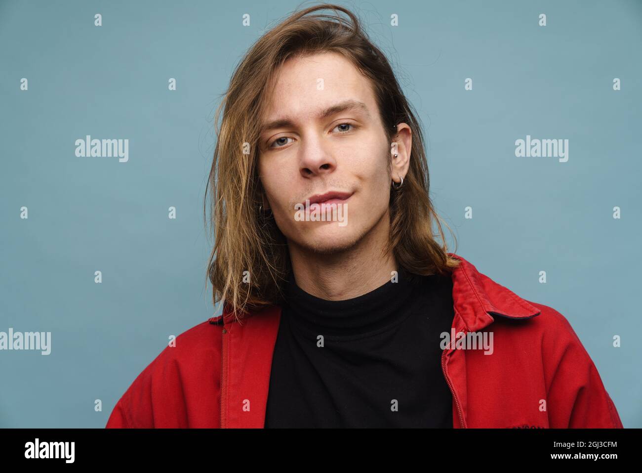 Porträt eines jungen blonden Mannes in einer Jacke, der auf blauem Hintergrund steht und die Kamera anschaut Stockfoto