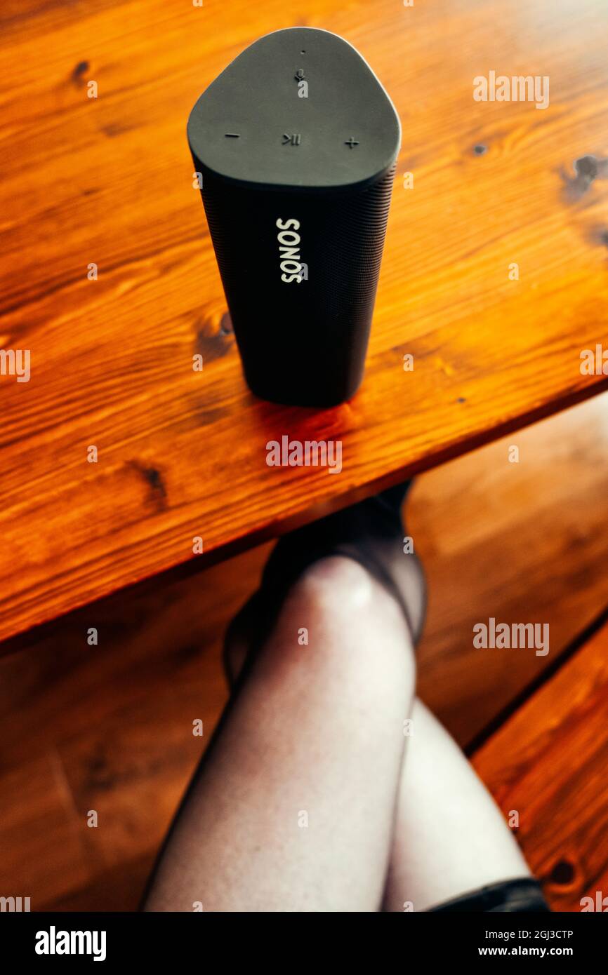 Sonos Roam tragbaren Lautsprecher auf einem Holztisch neben einer Frau saß mit gekreuzten Beinen Stockfoto