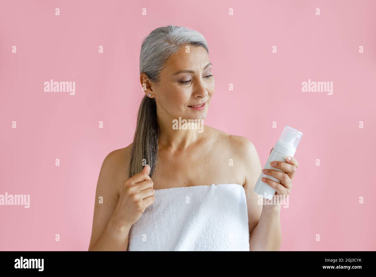 Schöne reife asiatische Dame mit Handtuch verpackt hält Flasche Körperpflegeprodukt im Studio Stockfoto