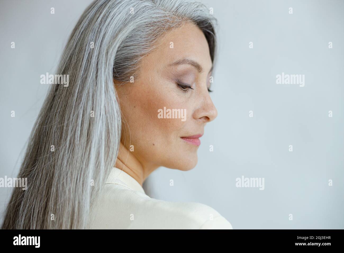 Hübsche asiatische Frau mittleren Alters mit lockeren geraden grauen Haaren auf hellem Hintergrund Stockfoto