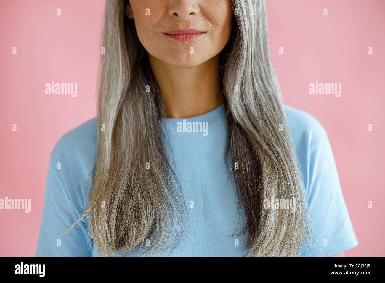 Positive Frau mittleren Alters mit langen, haarigen Haaren auf rosa Hintergrund Stockfoto