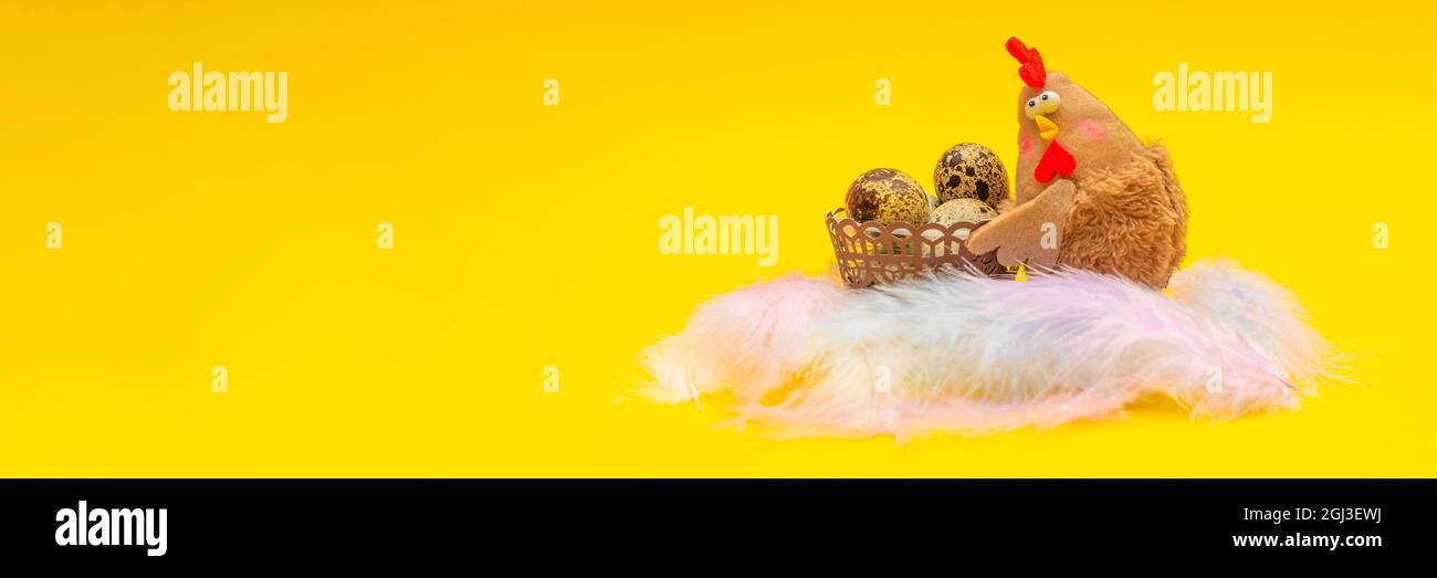 Huhn mit Ostereiern in einem Korb. Osterthema auf gelbem Hintergrund. Das Spielzeug-Huhn hält einen Korb mit Eiern. Ort für Ihren Text. Stockfoto