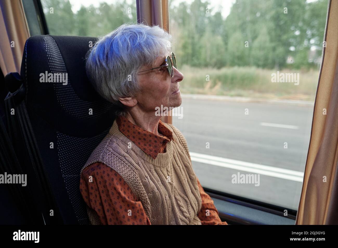 Seriöse ältere kaukasische Frau mit Sonnenbrille, die durch das Fenster schaut, während sie im Bus fährt Stockfoto