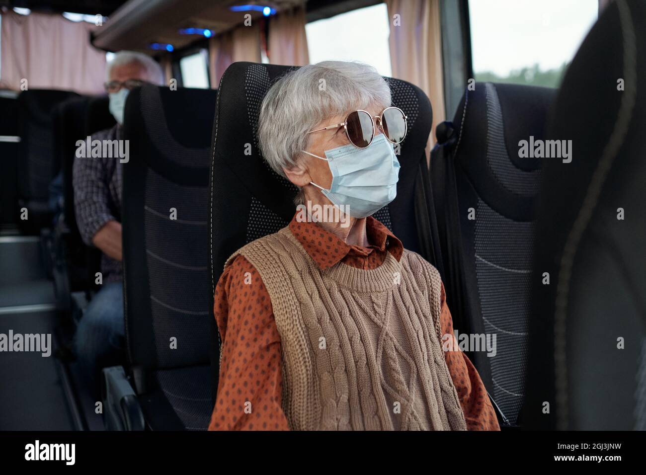 Ältere kaukasische Dame mit grauen Haaren, die Sonnenbrille und Gesichtsmaske trägt und im Bus sitzt Stockfoto