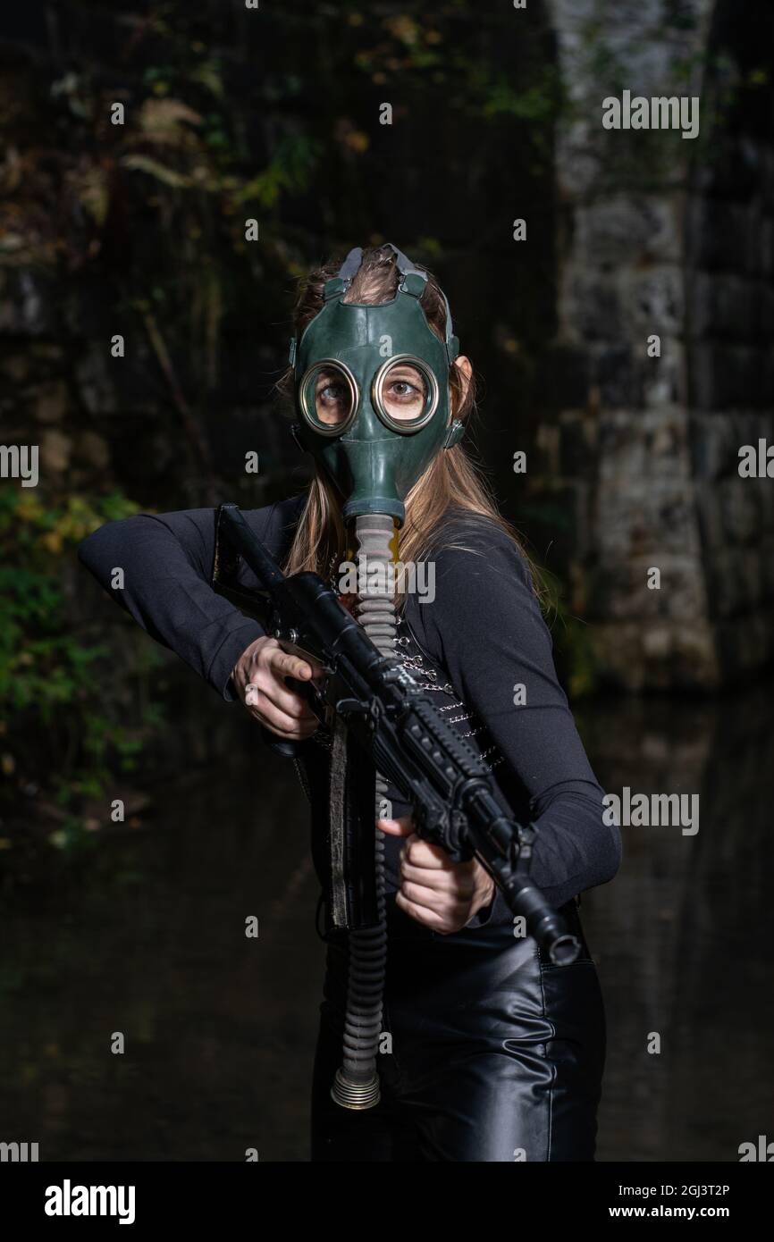 Eine Frau in einem schwarzen Anzug und einer Gasmaske mit einem Maschinengewehr in den Händen Stockfoto