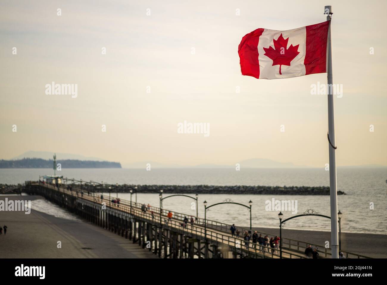 White Rock Stadtpier in der Abenddämmerung mit fliegender Flagge von Kanada, British Columbia, Kanada. Stockfoto