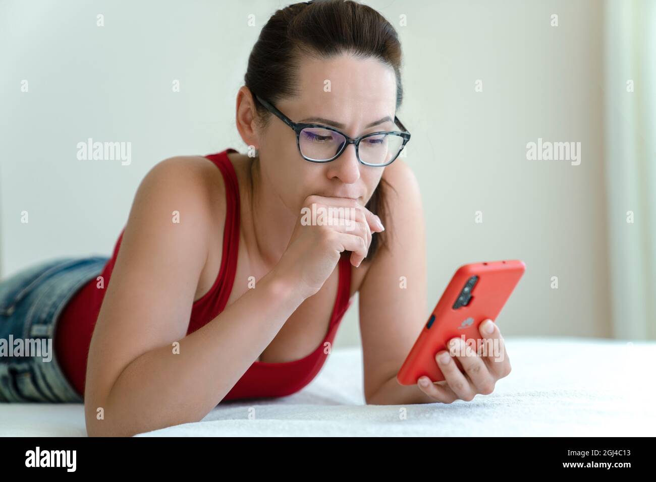 Frau spricht über eine Smartphone-Videokamera mit einem Blick auf Probleme auf ihrem Gesicht, während sie auf dem Bett liegt. Stockfoto
