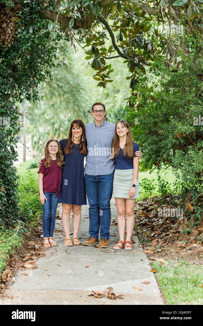 Eine Familie mit Mutter, Vater und zwei Töchtern, die im Sommer oder Herbst draußen auf dem Bürgersteig stehen Stockfoto