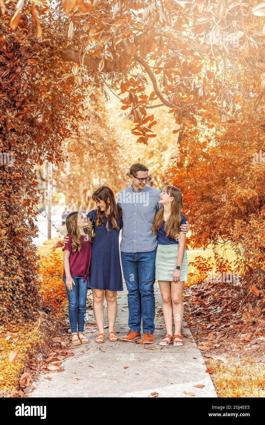 Eine Familie mit Mutter, Vater und zwei Töchtern, die im Herbst draußen auf dem Bürgersteig stehen Stockfoto