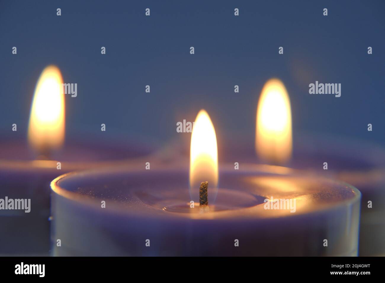 Brennende Kerzen im Dunkeln.Religionssymbol. Kerzen Hintergrund.Blaue Kerzen auf blauem Hintergrund Stockfoto