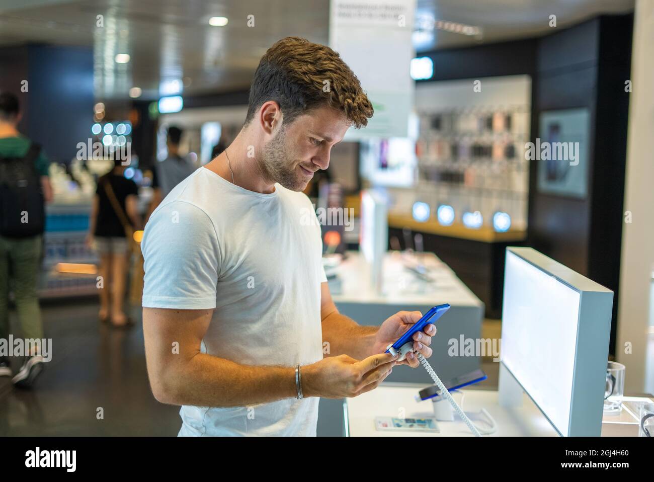 Seitenansicht des Inhalts junger bärtiger männlicher Käufer mit Mobiltelefon und lächelnd zufrieden mit der Qualität, während die Wahl neuer Gadget in modernen Elektronik-Shop Stockfoto