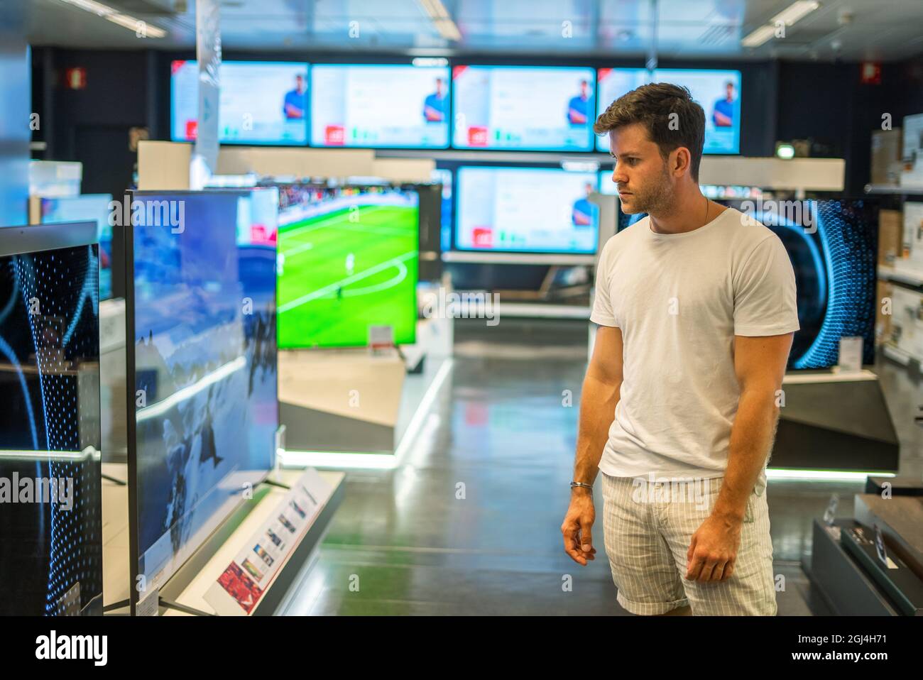 Junger männlicher Käufer in legerer Kleidung, der den modernen neuen großen Flachbildfernseher untersucht, während er ein Elektronikgeschäft besucht Stockfoto