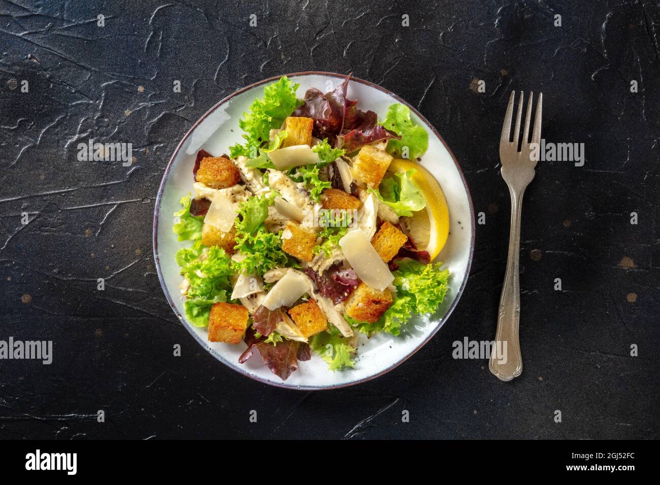 Chicken Caesar Salat, von oben auf schwarzem Hintergrund geschossen. Romaine-Blätter, knusprige Croutons, Hühnerfleisch und das klassische Dressing Stockfoto