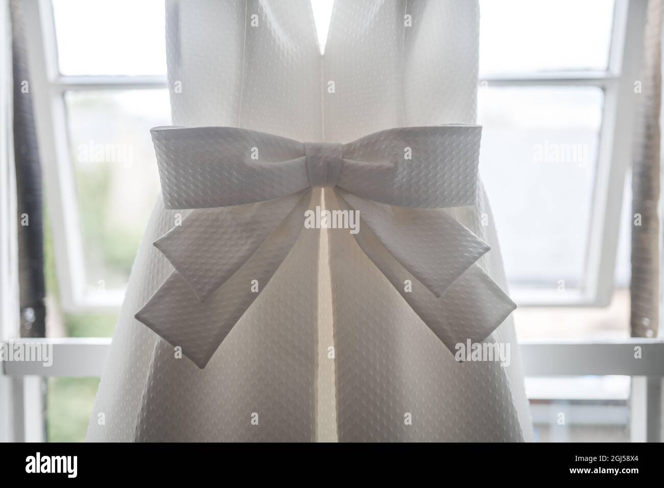 Schöne ziemlich große Schleife auf der Vorderseite der Bräute hell eleganten weißen Hochzeitskleid hängen im Fenster der Braut-Suite auf die Morgenzeremonie Stockfoto