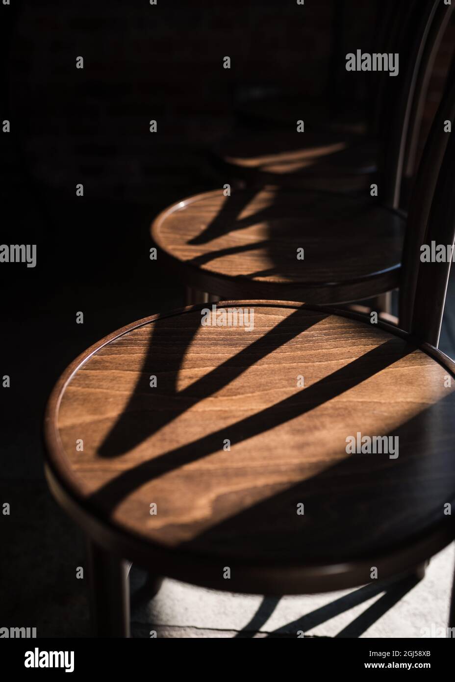 Die Sonne scheint über eine Reihe von Vintage-Holzsitzen und wirft Schatten in einem wunderschönen rustikalen, alten Hochzeitslokal. Keine Menschen, leer und ruhig. Stockfoto