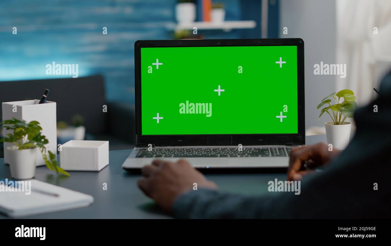 Nahaufnahme eines afroamerikanischen Mannes mit einem Laptop mit grünem Bildschirm im hellen Wohnzimmer. Computer-Usir mit isoliertem Chroma-Key-Mockup-Mock-Up-Display Stockfoto