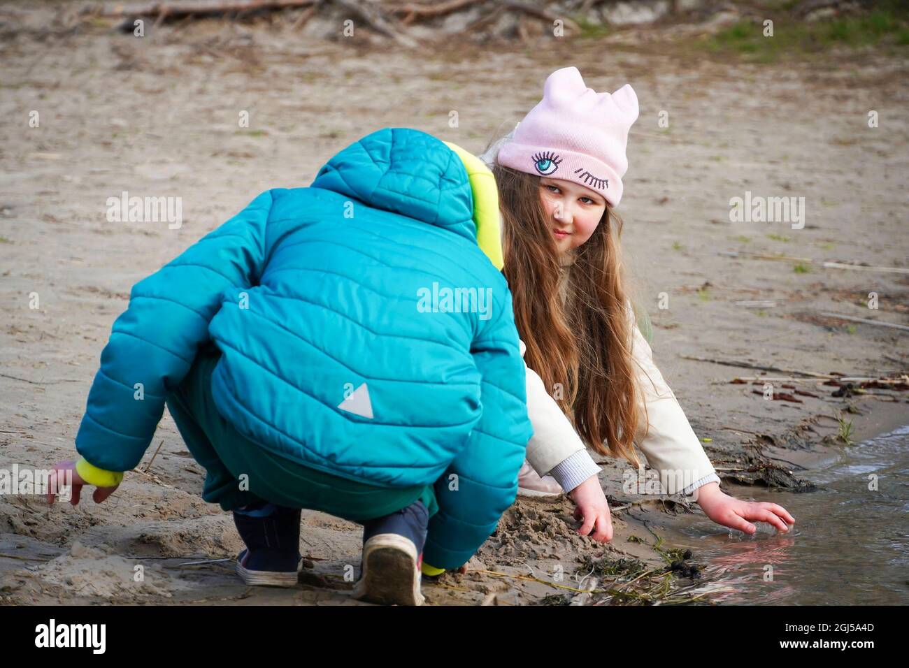 Ein kleines Mädchen und ein kleiner Junge, Schwester und Bruder, sitzen am Ufer des Flusses und spielen und berühren die Oberfläche des kalten Wassers. Kinder Geschwister spielen auf t Stockfoto