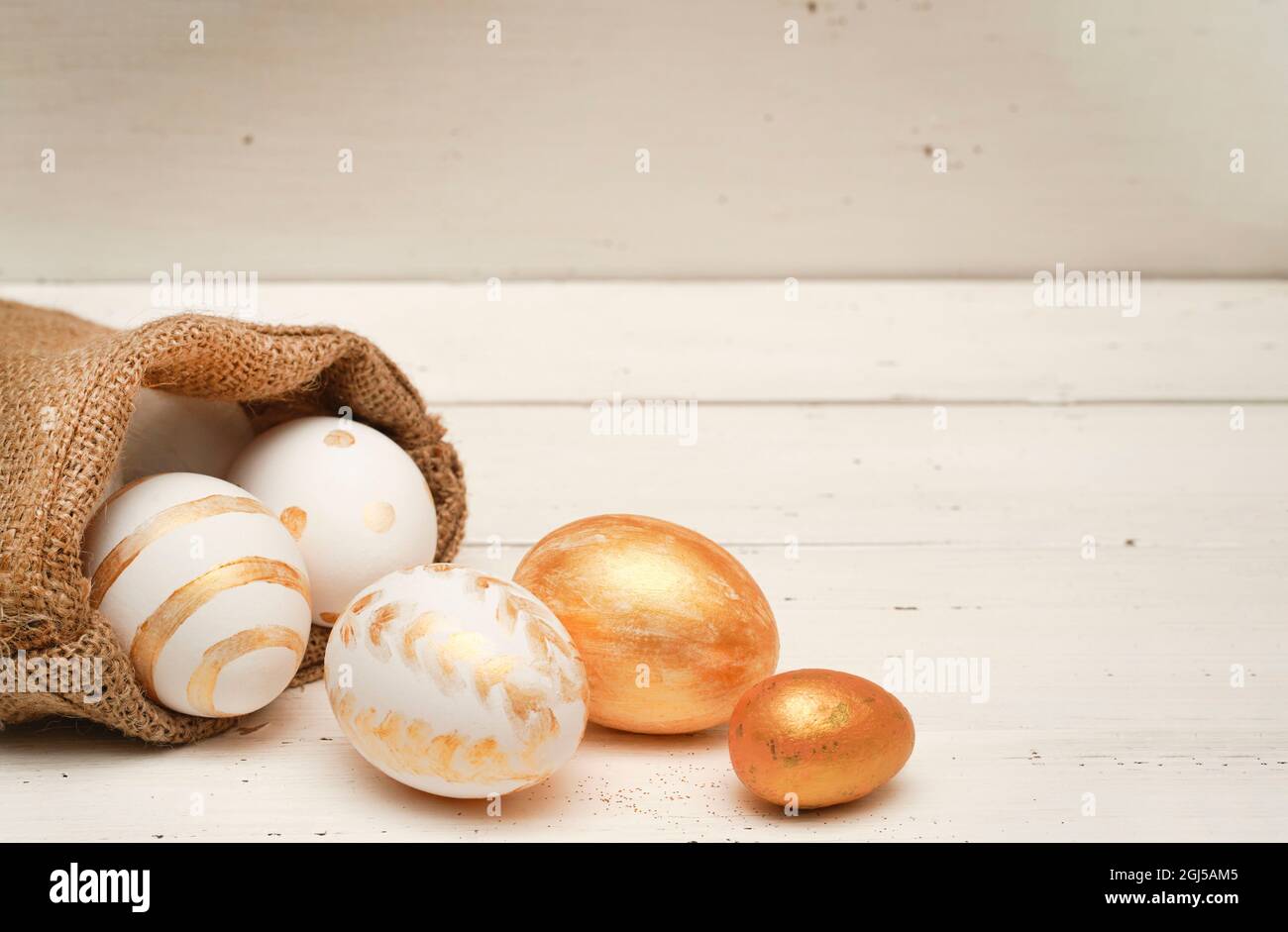 Goldene Ostereier in Jutebeutel auf rustikalem alten Holzhintergrund. Trendige Osterkomposition. Platz für Text kopieren. Minimales Osterkonzept. Stockfoto