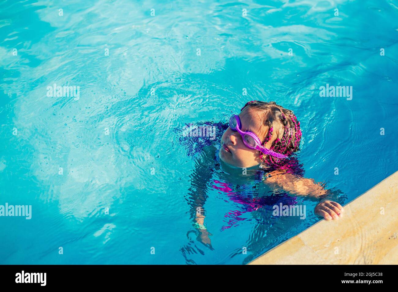 Ein Mädchen in einer Schwimmbrille hat Spaß und spritzt im Pool. Stockfoto