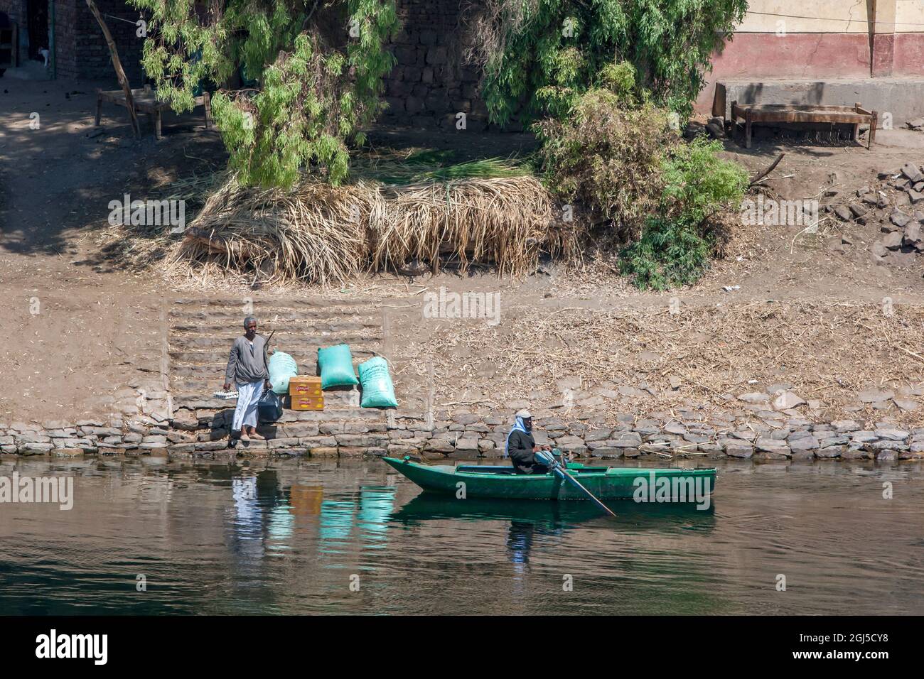 Ein Mann wartet am Ufer des Nils mit Lebensmitteln, die von einem Ruderboot südlich von Edfu in Zentralägypten abgeholt werden. Stockfoto