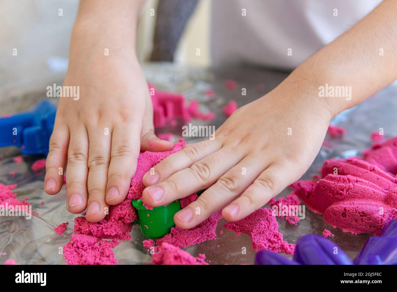 Nahaufnahme der Hände des Kindes, die im kinetischen Sand spielen. Selektive Fokusaufnahme der Hände des Kindes mit rotem kinetischem Sand und verschiedenen Farbformen Stockfoto