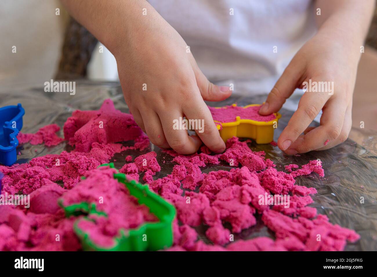 Nahaufnahme der Hände des Kindes, die im kinetischen Sand spielen. Selektive Fokusaufnahme der Hände des Kindes mit rotem kinetischem Sand und verschiedenen Farbformen Stockfoto