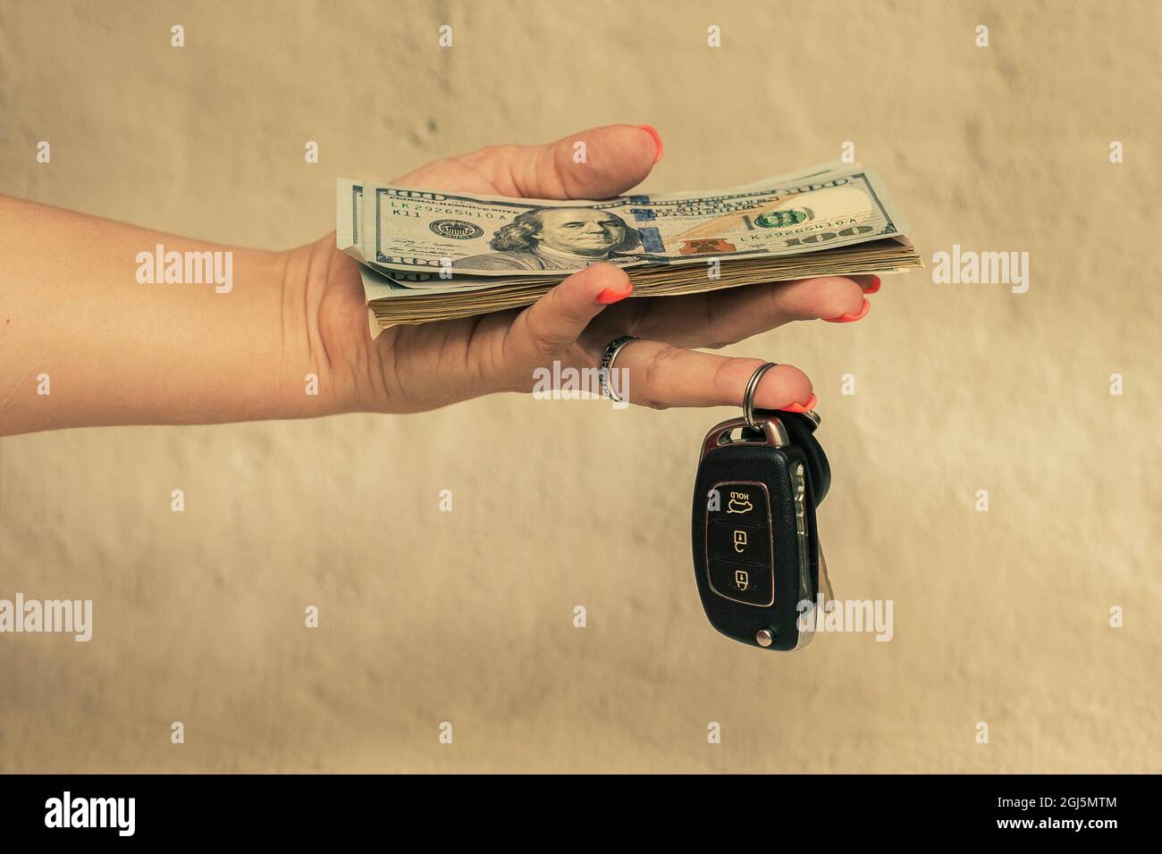 Dollar und schwarze Autoschlüssel in der Hand einer Frau. Stockfoto