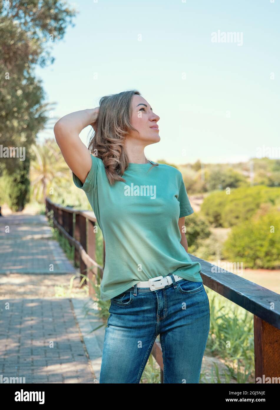 Frauen mittleren Alters, die T-Shirt und Jeans tragen, bleiben im Park mit der Hand über den Kopf Stockfoto