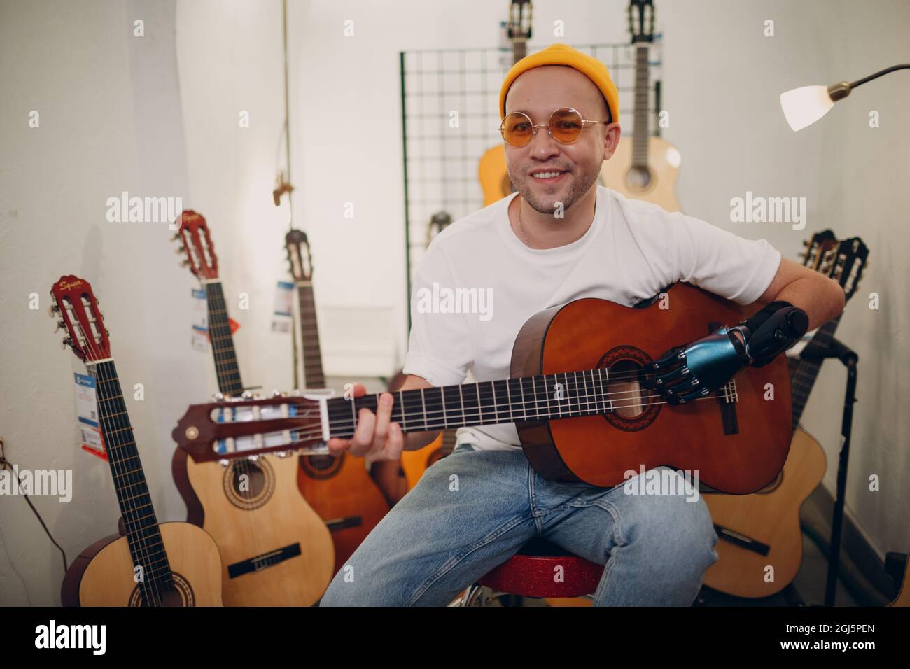 Junger behinderter Mann mit künstlicher prothetischer Hand spielt auf der Gitarre im Geschäft Stockfoto