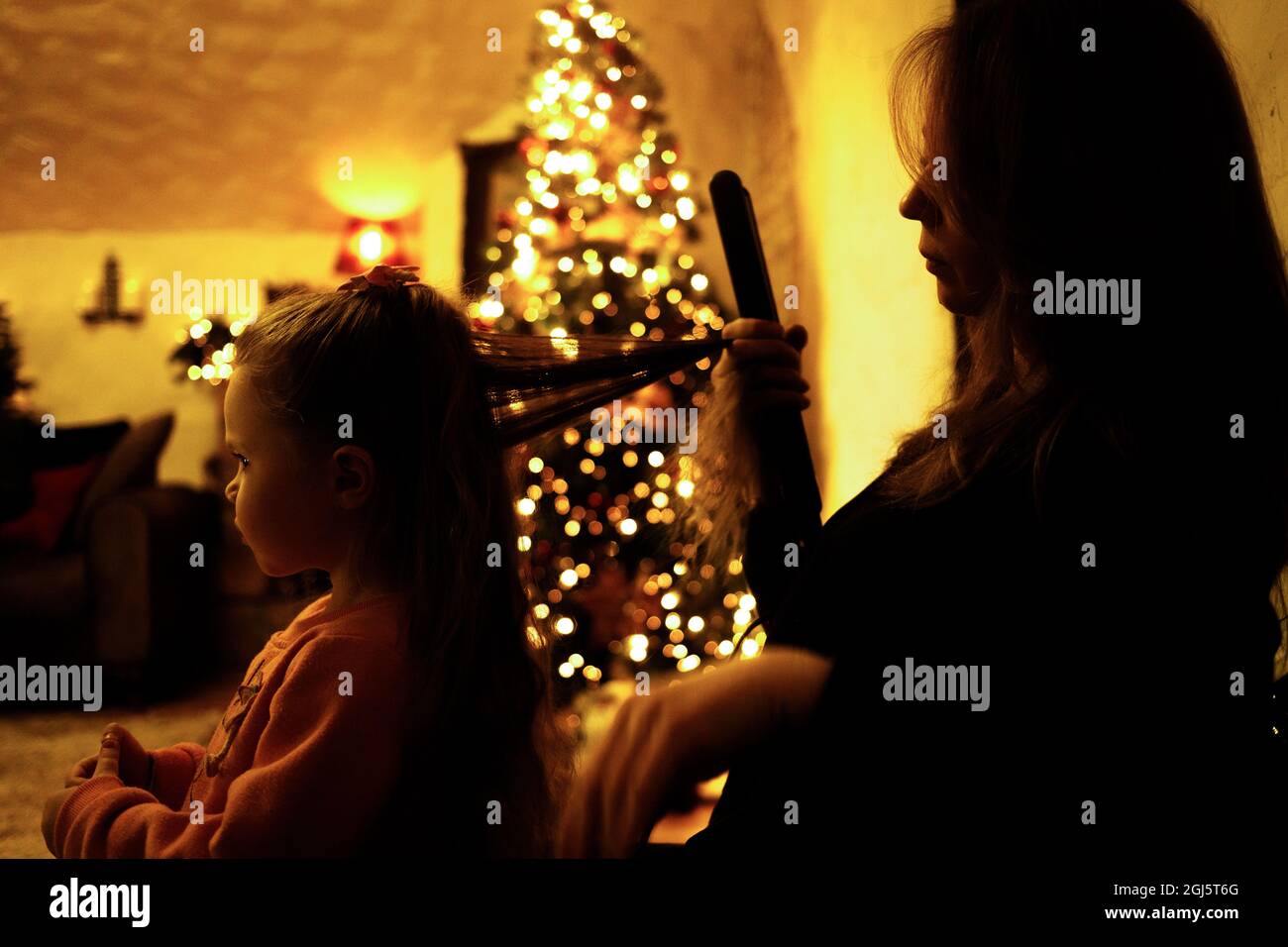 Mutter kämmt ihre Tochter zu einem festlichen Abendessen im Zimmer mit einem weihnachtsbaum. Selektiver Weichfokus, Filmkorneffekt Stockfoto