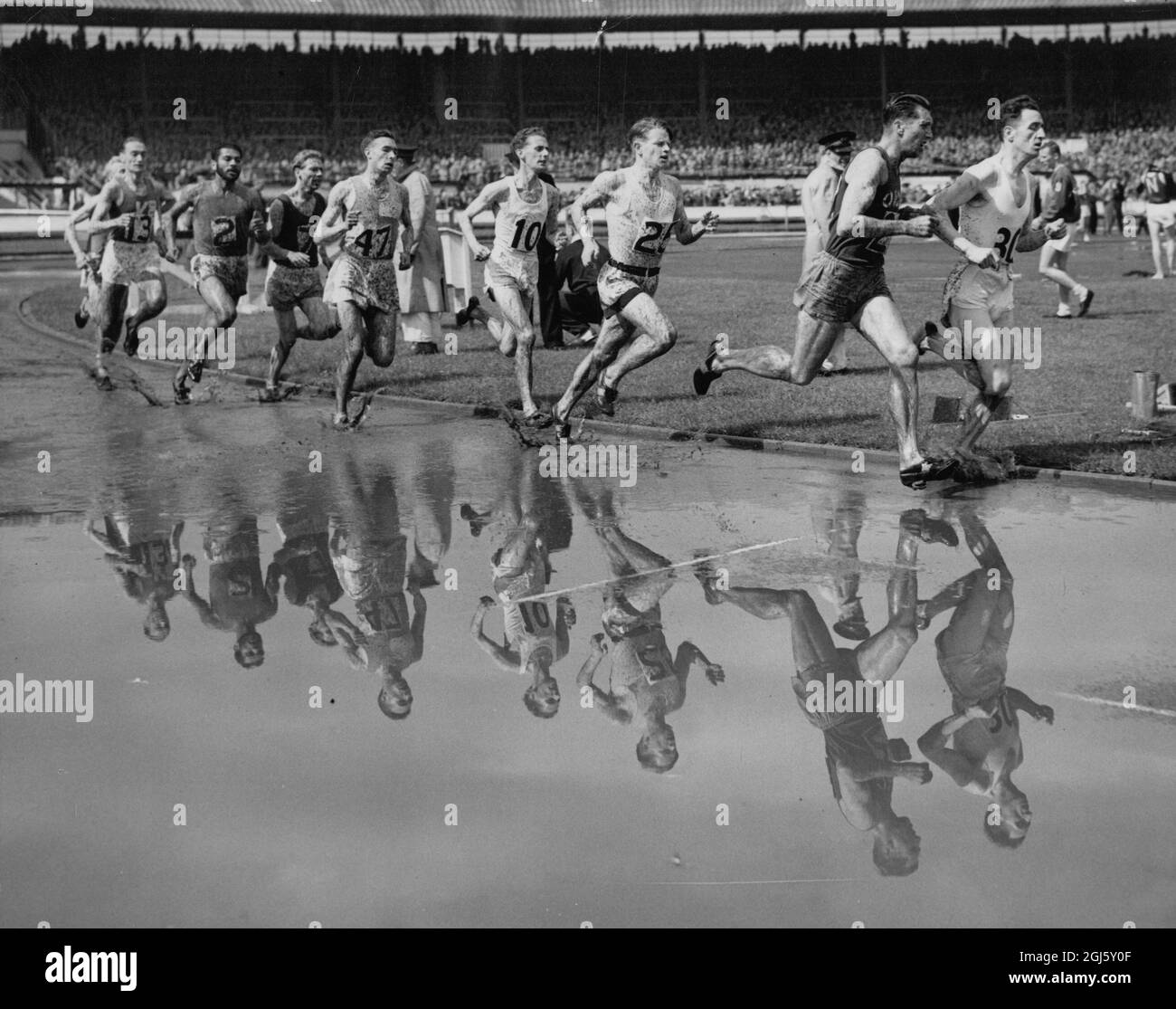 Die wasserdurchlaufte Strecke in der White City, London, spiegelt die Läufer beim Milelauf bei den British Games wider. Die Veranstaltung wurde von Chris Chataway von Surrey gewonnen. Juni 1952 Stockfoto
