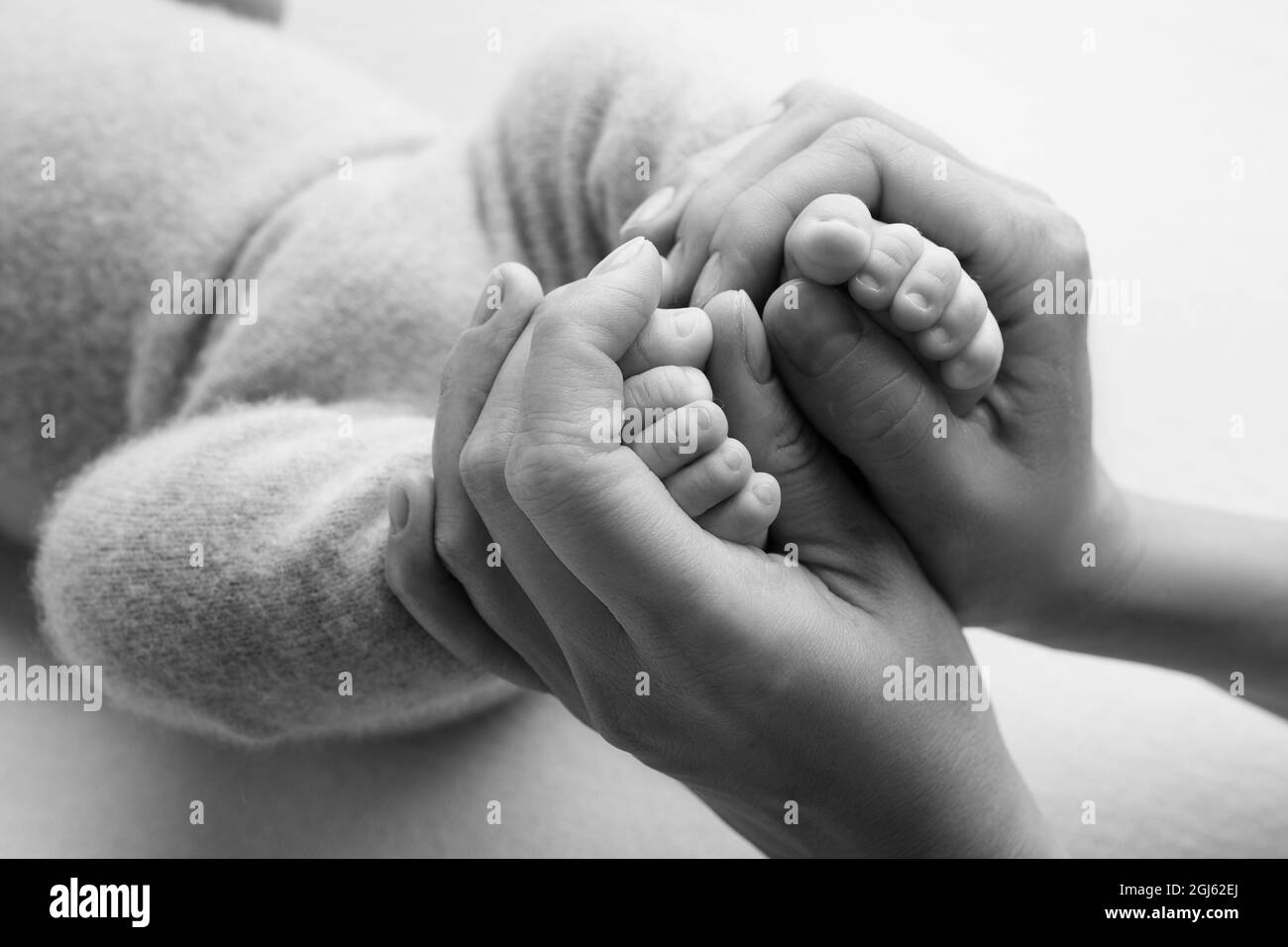 Foto mit Kinderbeinen, die in den Handflächen von Mama und Papa gehalten werden. Schwarz-Weiß-Foto. Familienalbum. Neugeborene Füße. Stockfoto