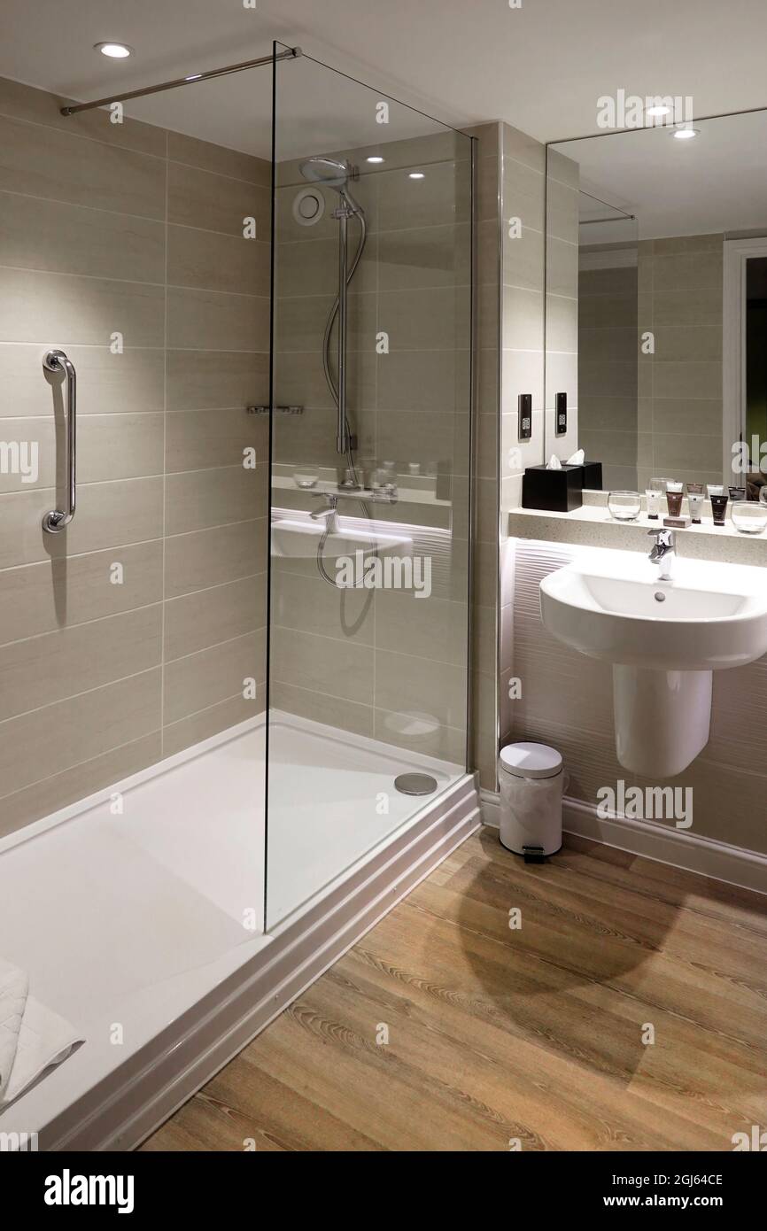 Moderne, begehbare gekachelte Dusche und große Sicherheitsschiene im eigenen Hotelbadezimmer, Spiegel in voller Höhe über dem an der Wand montierten Waschhandwaschbecken England Großbritannien Stockfoto