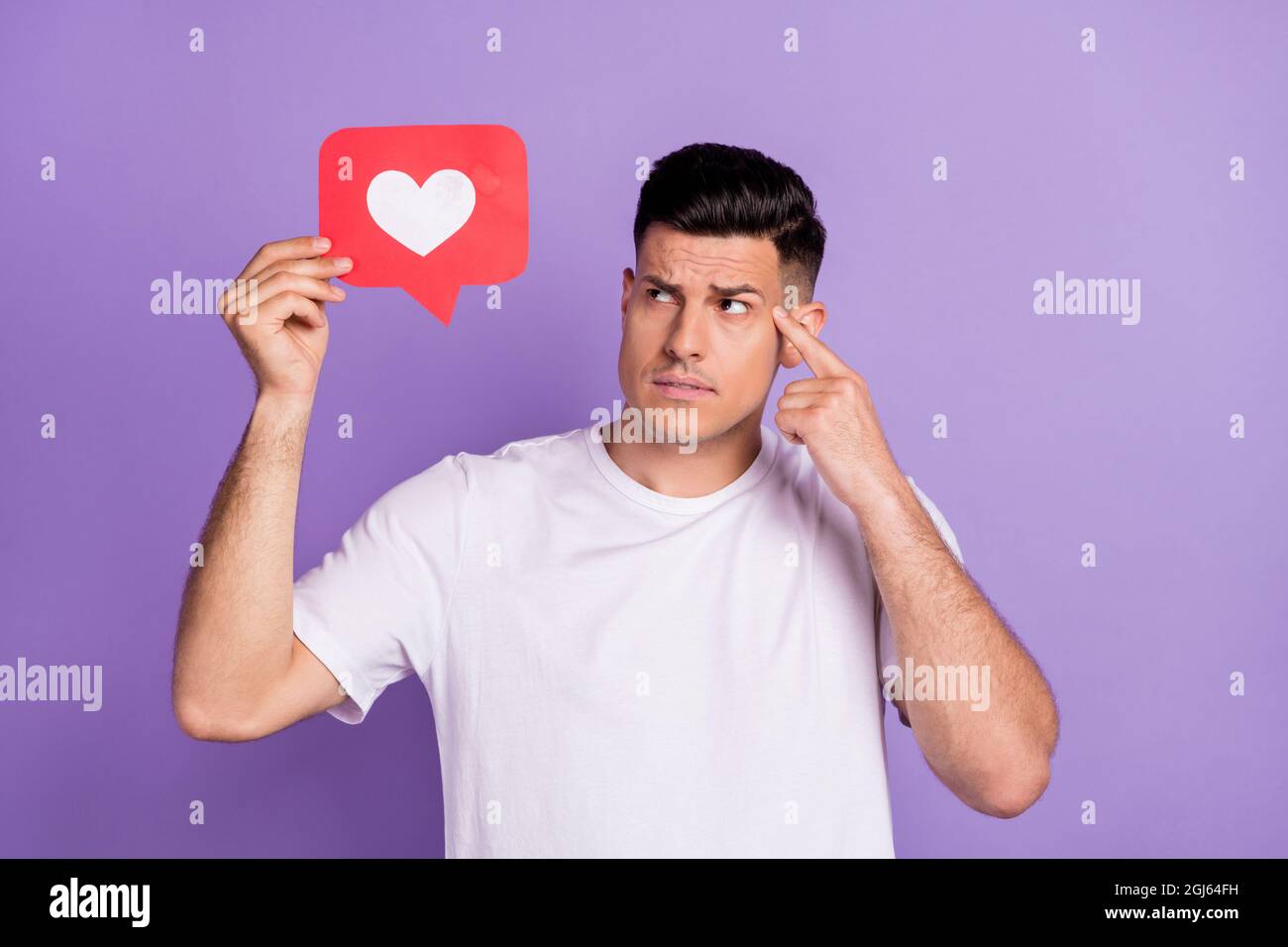 Foto von gesinnten jungen nachdenklichen Mann Blick halten Hand Herz Symbol Finger Kopf isoliert auf violettem Hintergrund Stockfoto