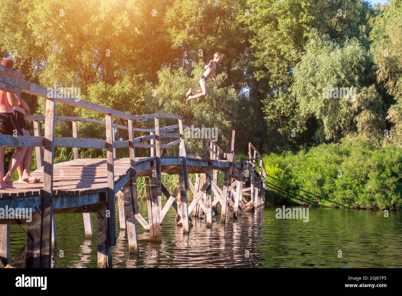 Der Junge springt von einer Holzbrücke ins Wasser Stockfoto