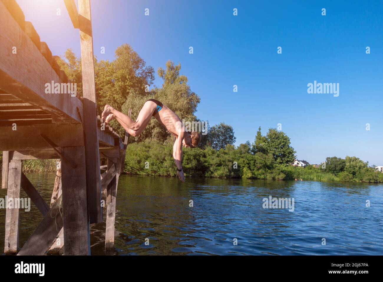 Der Junge springt von einer Holzbrücke ins Wasser Stockfoto