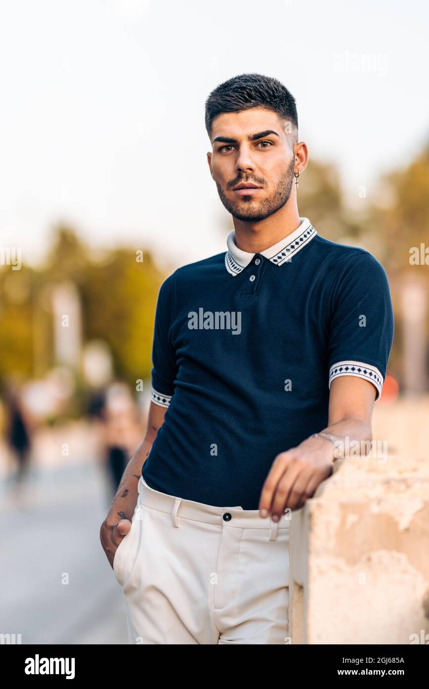 Vertikales Foto eines jungen Mannes in moderner Sommerkleidung, der an einer Wand lehnt Stockfoto