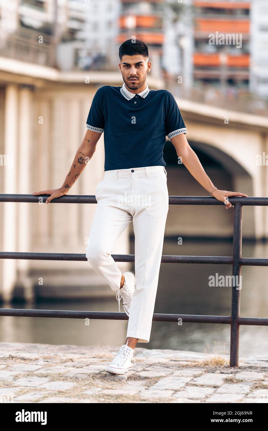 Vertikales Foto eines jungen Mannes in moderner Kleidung, der auf einer Schiene lehnt Stockfoto