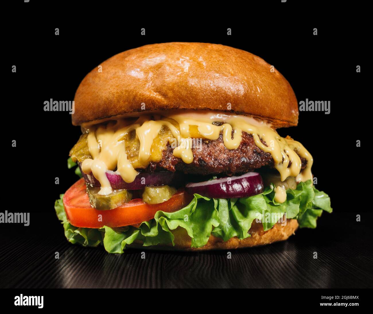 Handwerk Burger ist Kochen auf schwarzem Hintergrund in Schwarz essen Handschuhe. Bestehen: Sauce, Salat, Tomaten, Roten Zwiebeln, Gurke, Käse, Speck, Brötchen und marbl Stockfoto