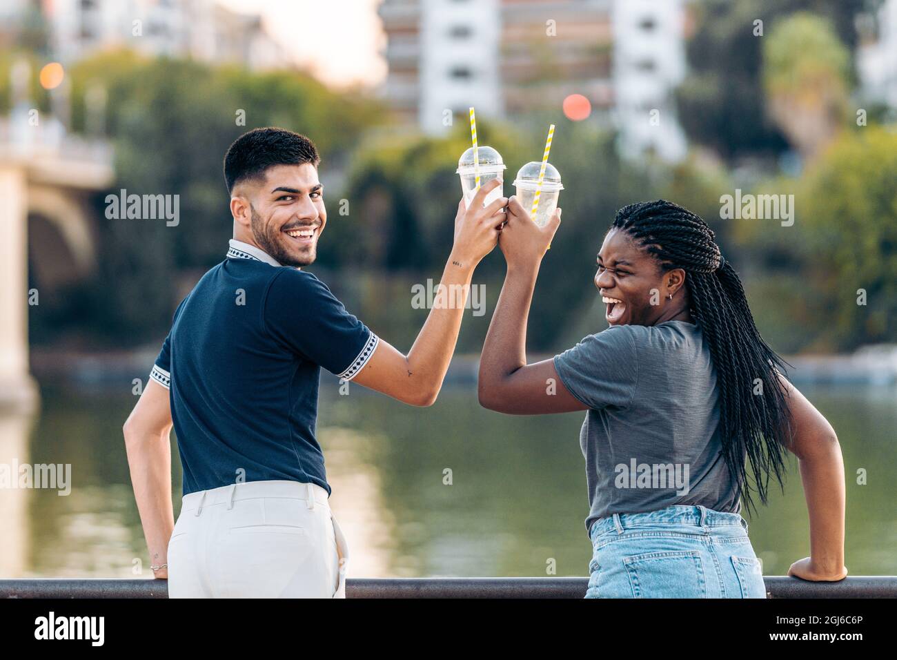 Zwei multiethnische Menschen toasten mit einem Shake, während sie im Freien lachen Stockfoto