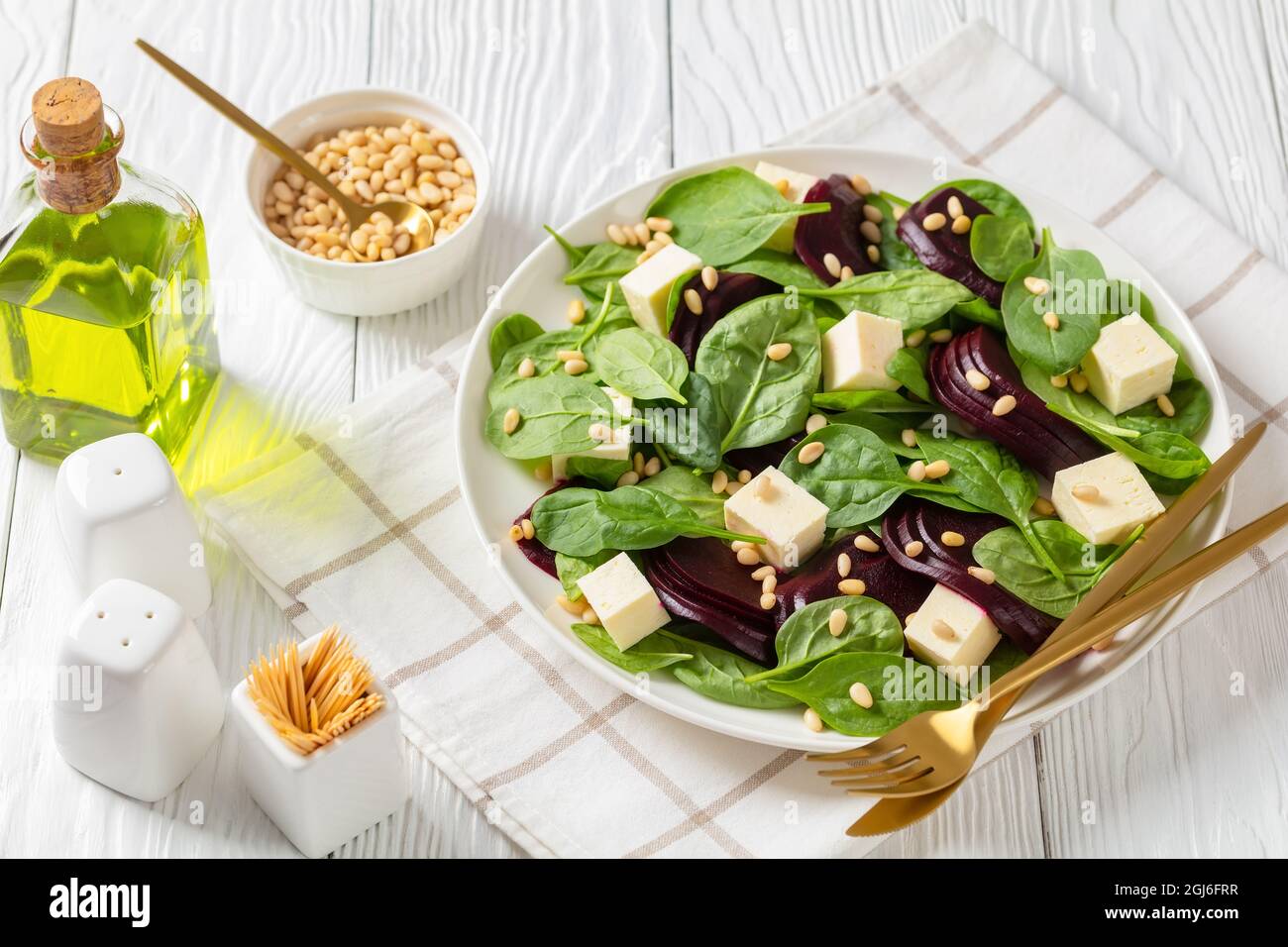 Gerösteter Rübensalat mit gewürfeltem Feta-Käse, Pinienkernen und Spinat auf einem weißen Teller mit goldenem Besteck auf einem Holztisch, kanadische Küche Stockfoto