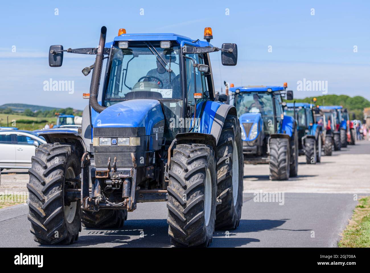 Eine Reihe blauer New Holland-Traktoren beginnt eine Traktorenfahrt, die üblicherweise in ländlichen Gebieten Irlands stattfindet, um Geld für Wohltätigkeitsorganisationen zu sammeln. Stockfoto