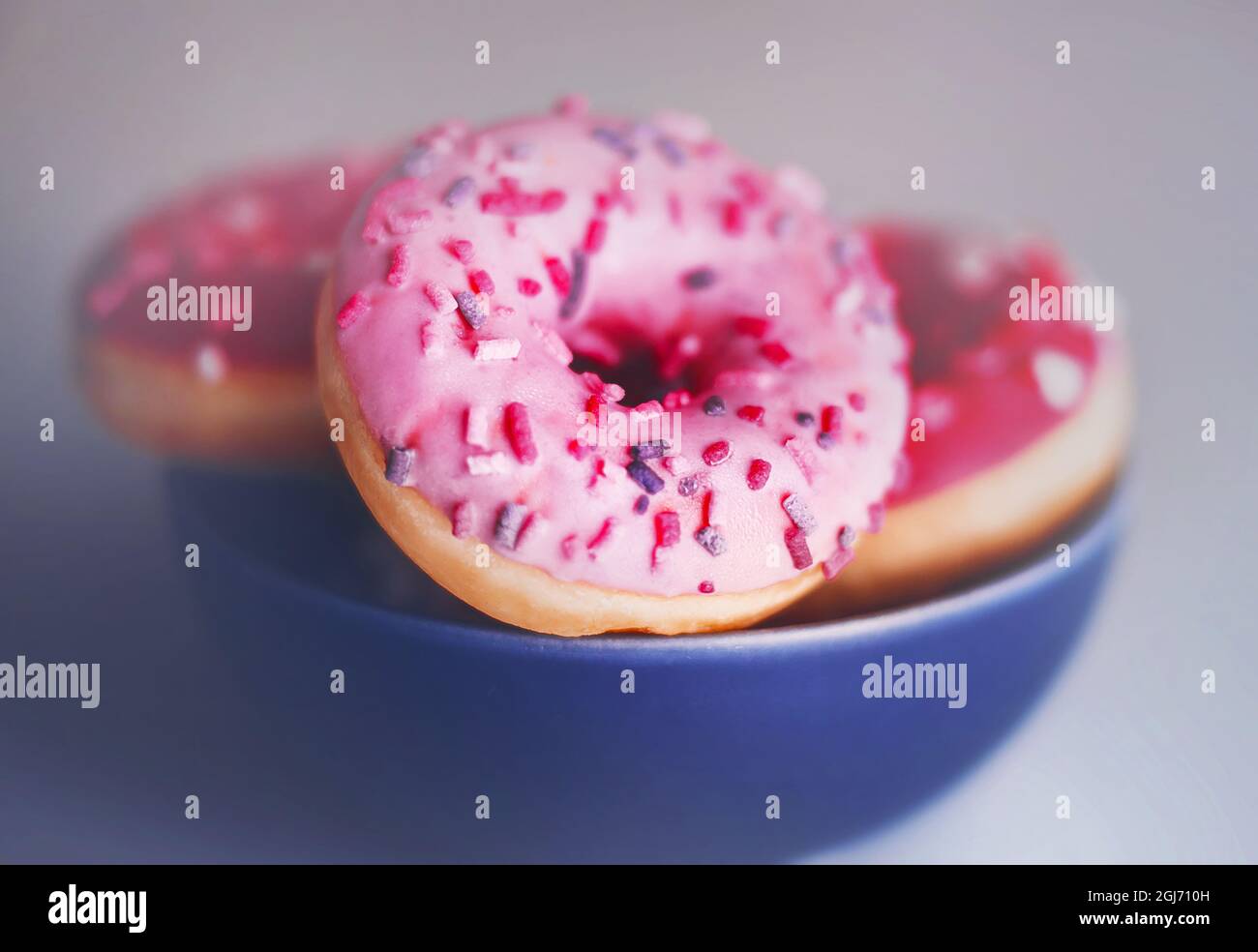 In einem blauen Teller gibt es mehrere rosafarbene leckere Donuts mit Erdbeerfüllung. Dessert für den Urlaub. Junk Food. Stockfoto