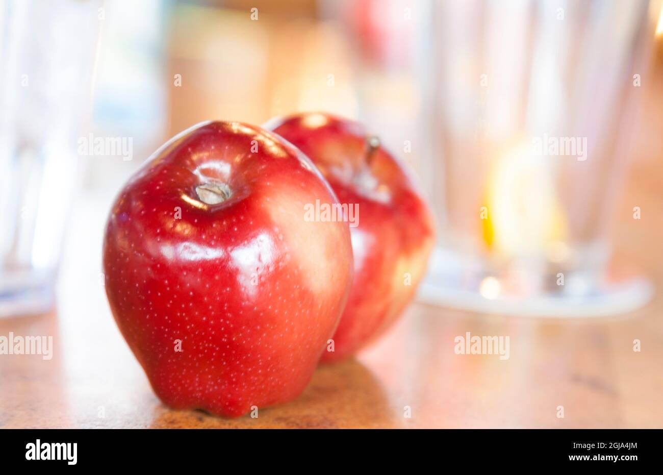 Gesunde rote Äpfel auf einem Tisch mit Wassergläsern im Hintergrund. Stockfoto